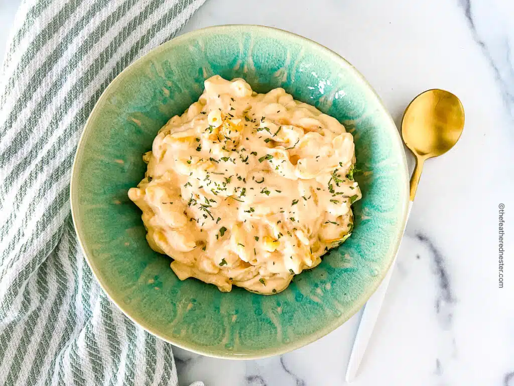 horizontal photo of slow cooker mac and cheese with cream cheese in a green bowl with a spoon at the side.