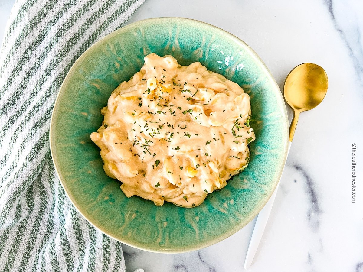 A bowl of mac and cheese with dish towel and gold spoon on the side