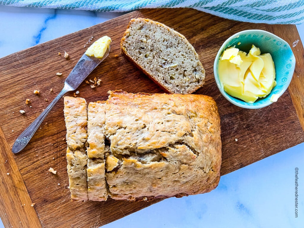 a sliced loaf of banana bread on a wooden board with a bowl of butter to the side