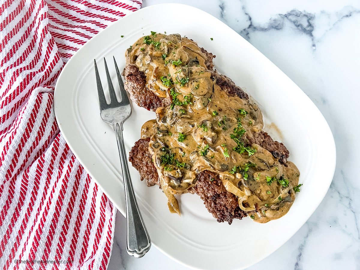 crock pot cube steak in a white plate with fork and a dish towel on the side