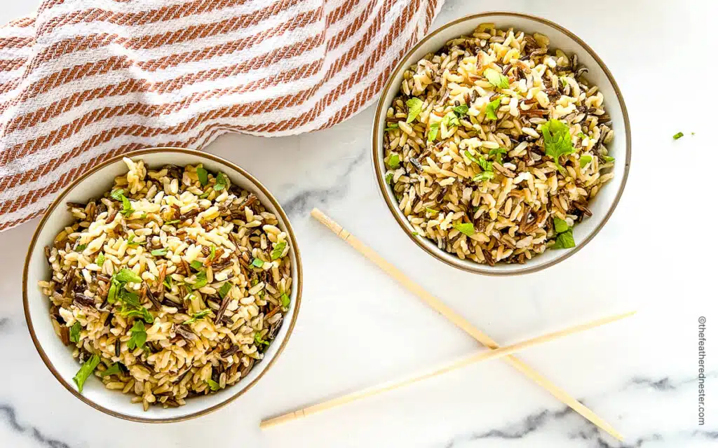two bowls with cooked wild rice, chopsticks between the bowls, and a striped red kitchen towel behind them.
