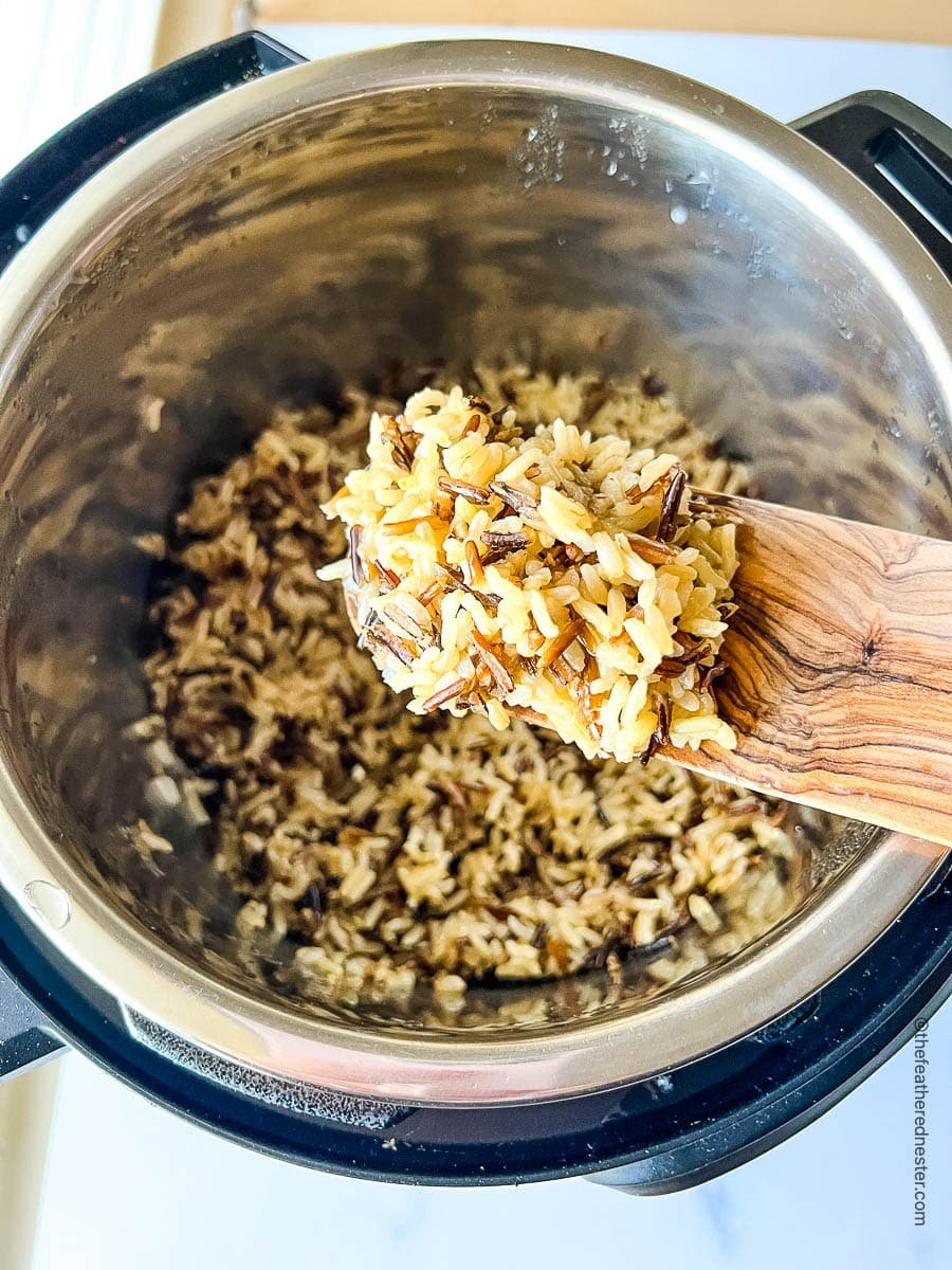Fluffy cooked grains on a wooden spatula above pressure cooker.
