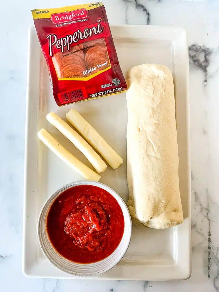 Ingredients needed for making Mini Pepperoni Calzones which consist of Bridgford pepperoni, string cheese, Bridgford's Ready-Dough, and marinara sauce.