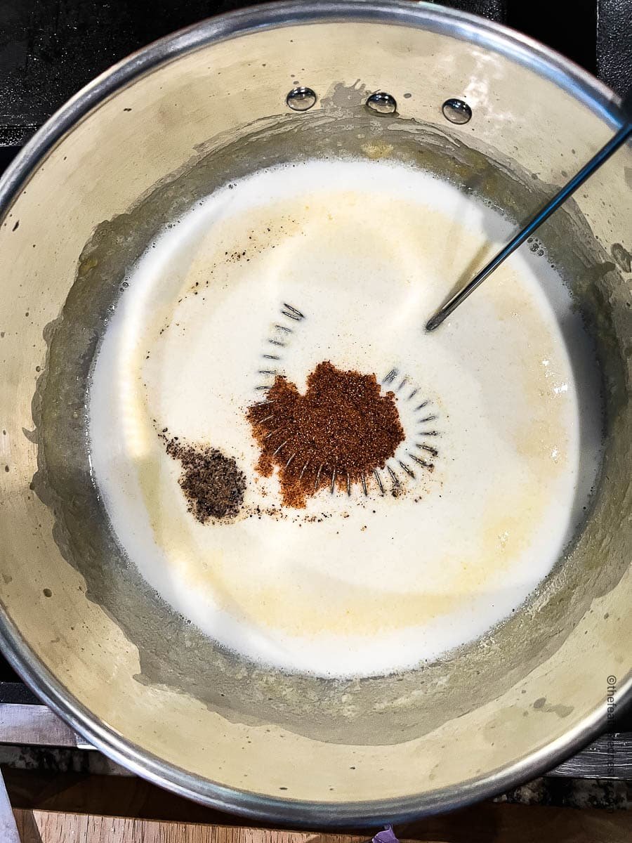 whisking ground spices into pot of bechamel sauce.