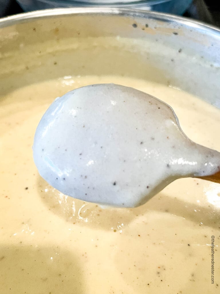 cooked bechamel cheese sauce coating the back of a spoon above a saucepan.