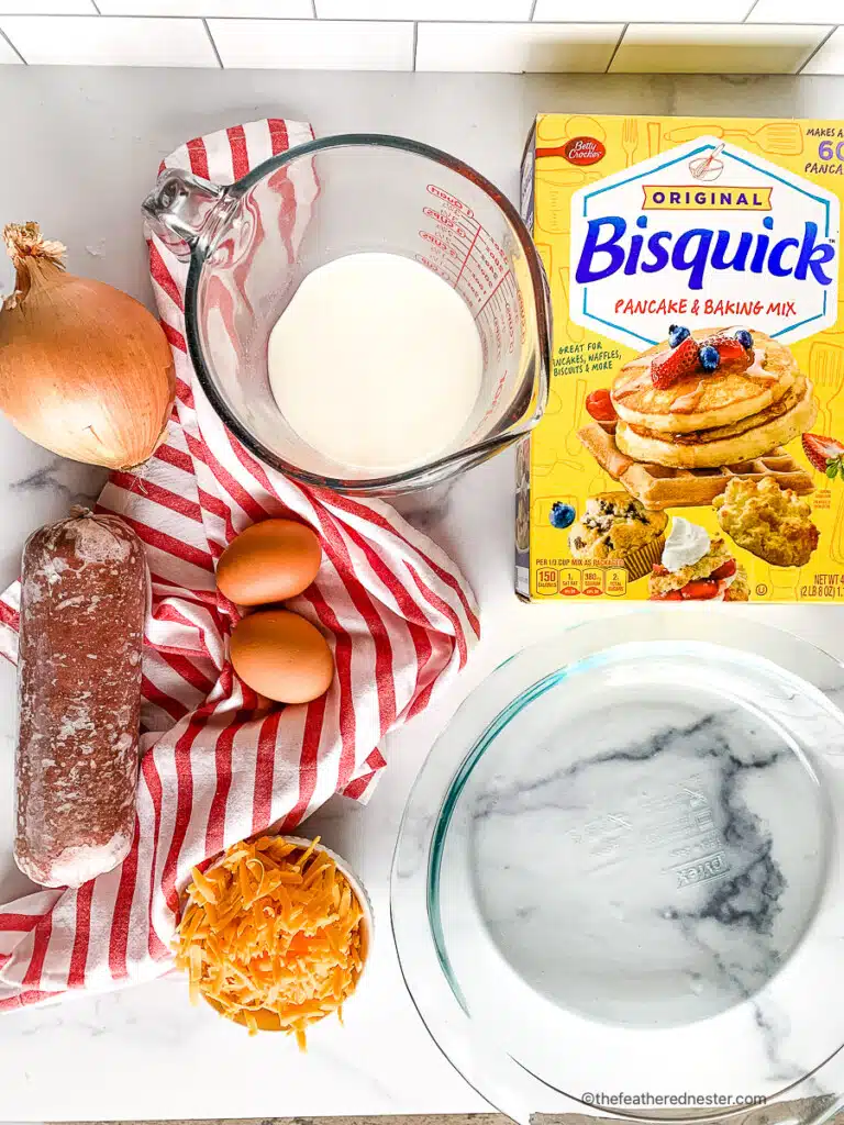 Box of Original Bisquick baking mix next to eggs, milk, onion, shredded cheese and ground beef for a cheeseburger pie recipe.