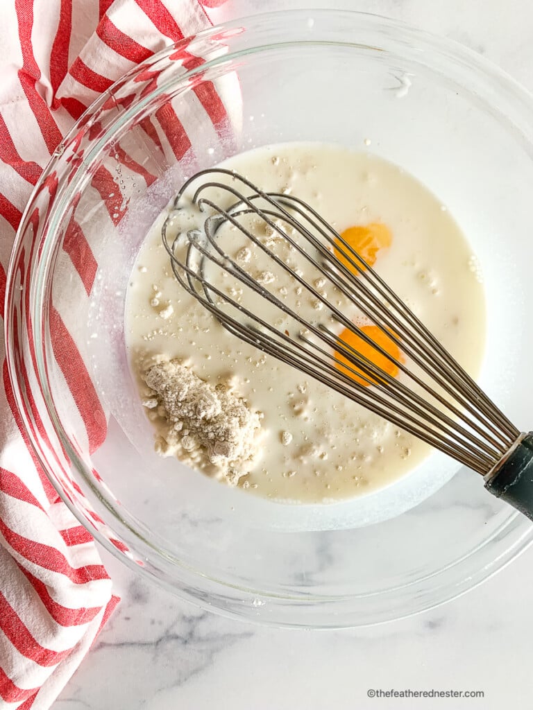 Using a whisk to combine eggs with milk and baking mix in a glass mixing bowl.