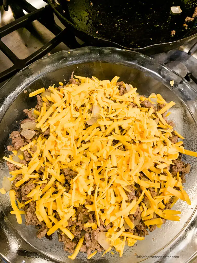 shredded cheddar cheese on top of ground beef in a glass baking dish.