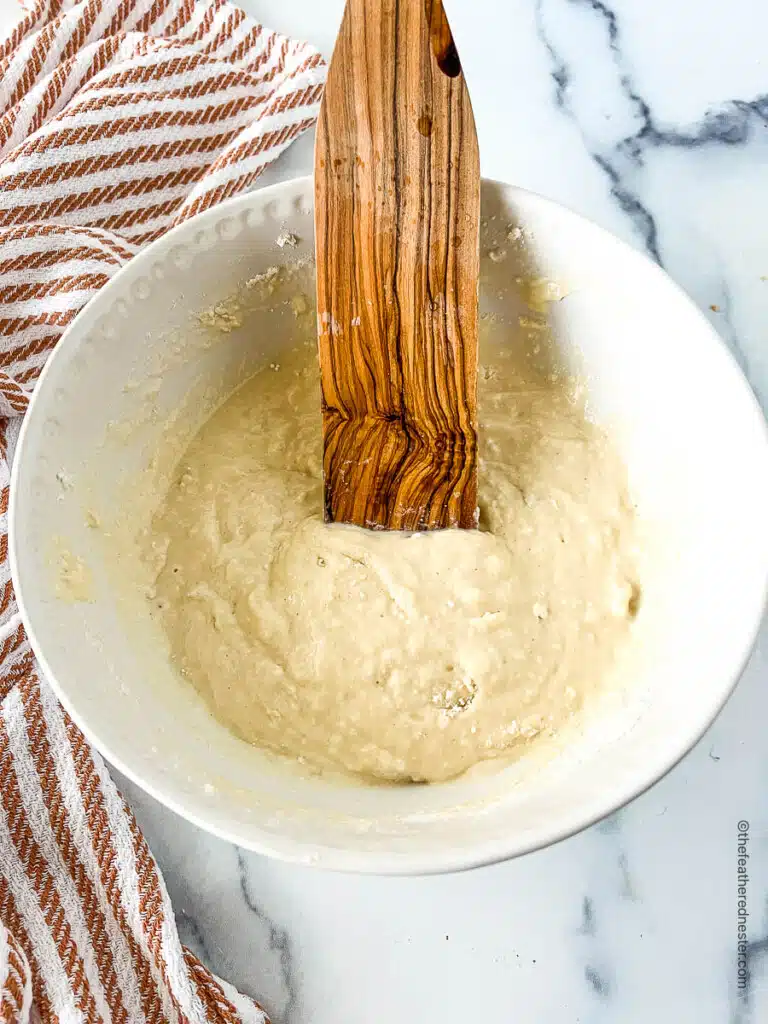 large wooden spoon stirring thick white batter in a bowl.