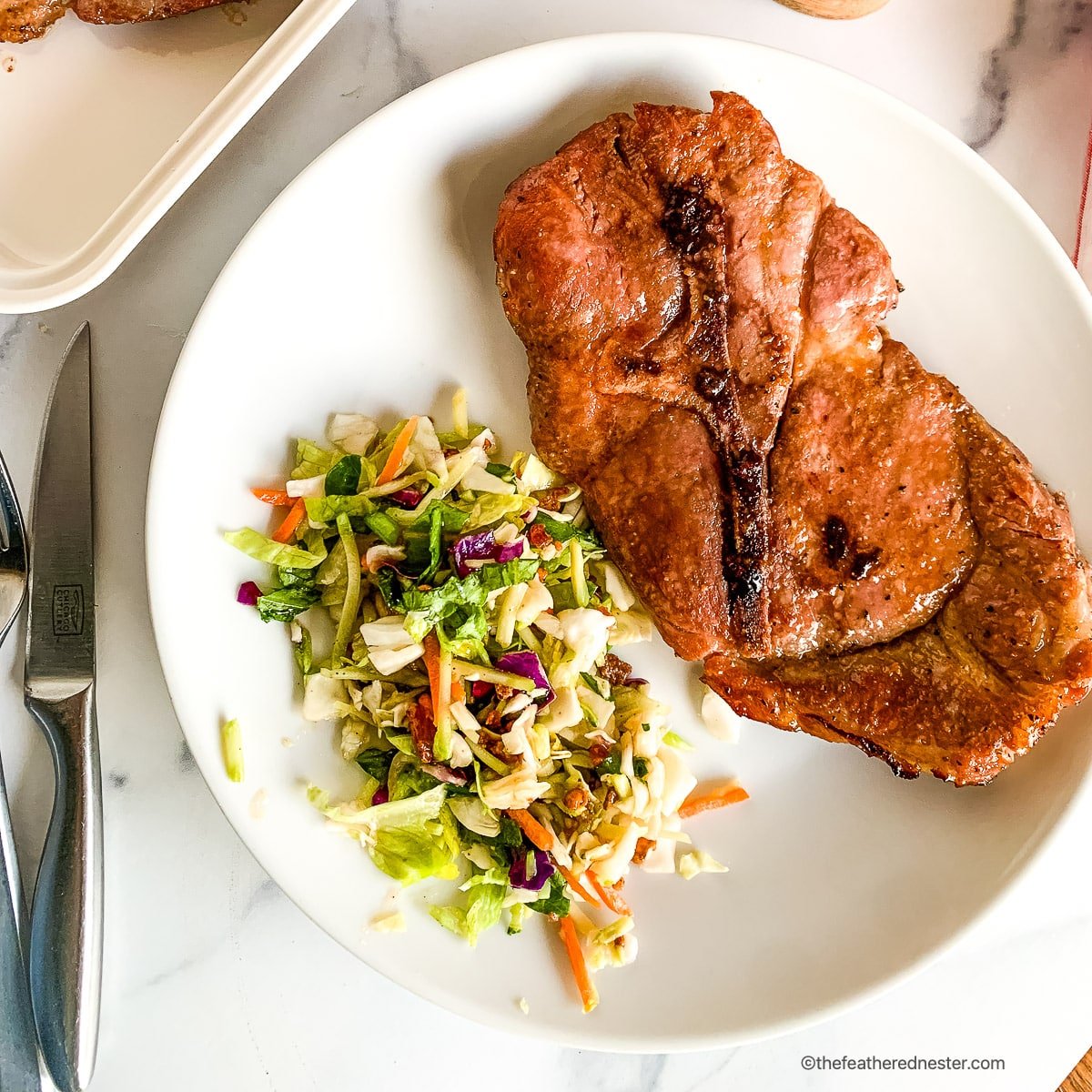 Oven baked pork steak dinner on a round white plate.