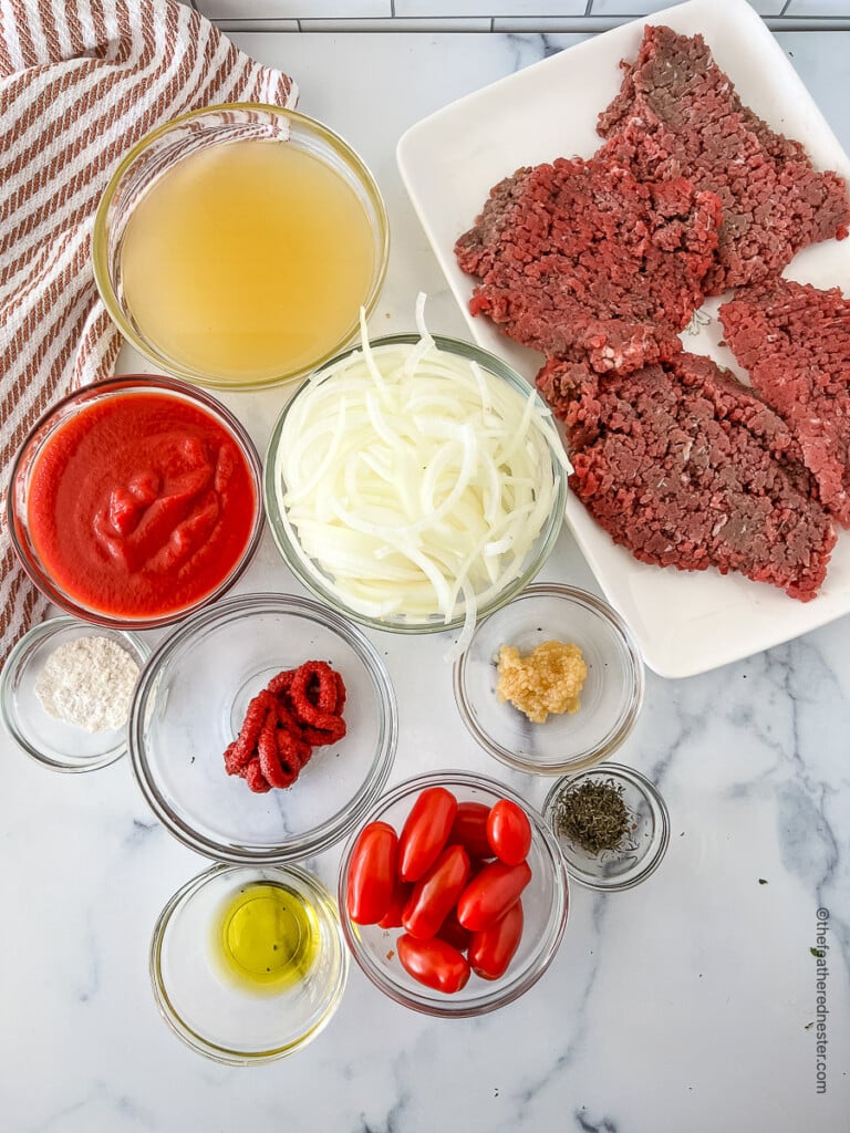 ingredients needed for making Crock pot Swiss steak recipe: cube steaks, chicken broth, tomato puree, onions, tomato paste, minced garlic, dried thyme, olive oil, all-purpose flour, and cherry tomatoes.