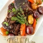 a white serving plate with Dutch Oven Pot Roast and vegetables. with writings at the bottom part that says "dutch oven pot roast www.thefeatherednester.com".