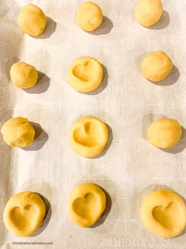 unbaked thumbprint heart cookies on parchment lined baking sheet