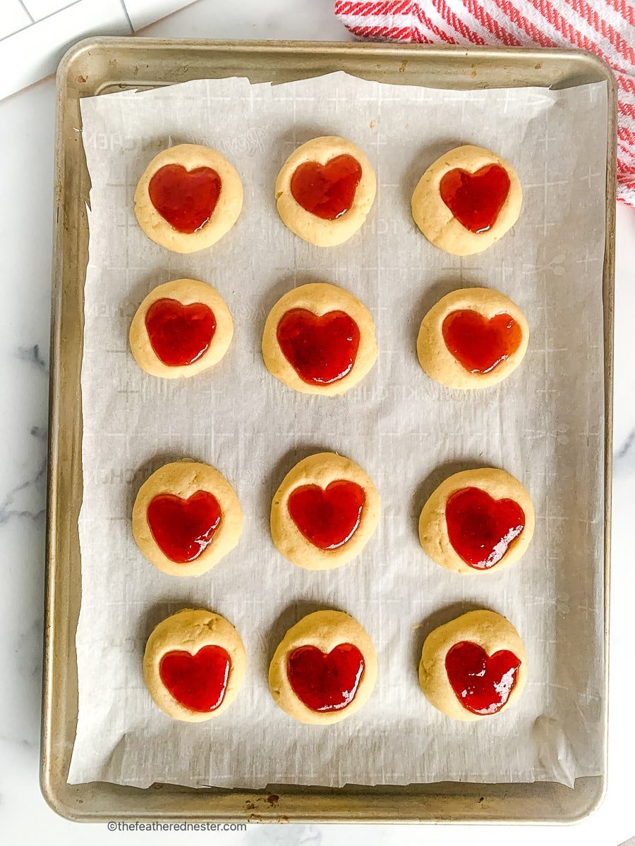 cookies with jam thumbprints placed on a parchment paper lined baking sheet.