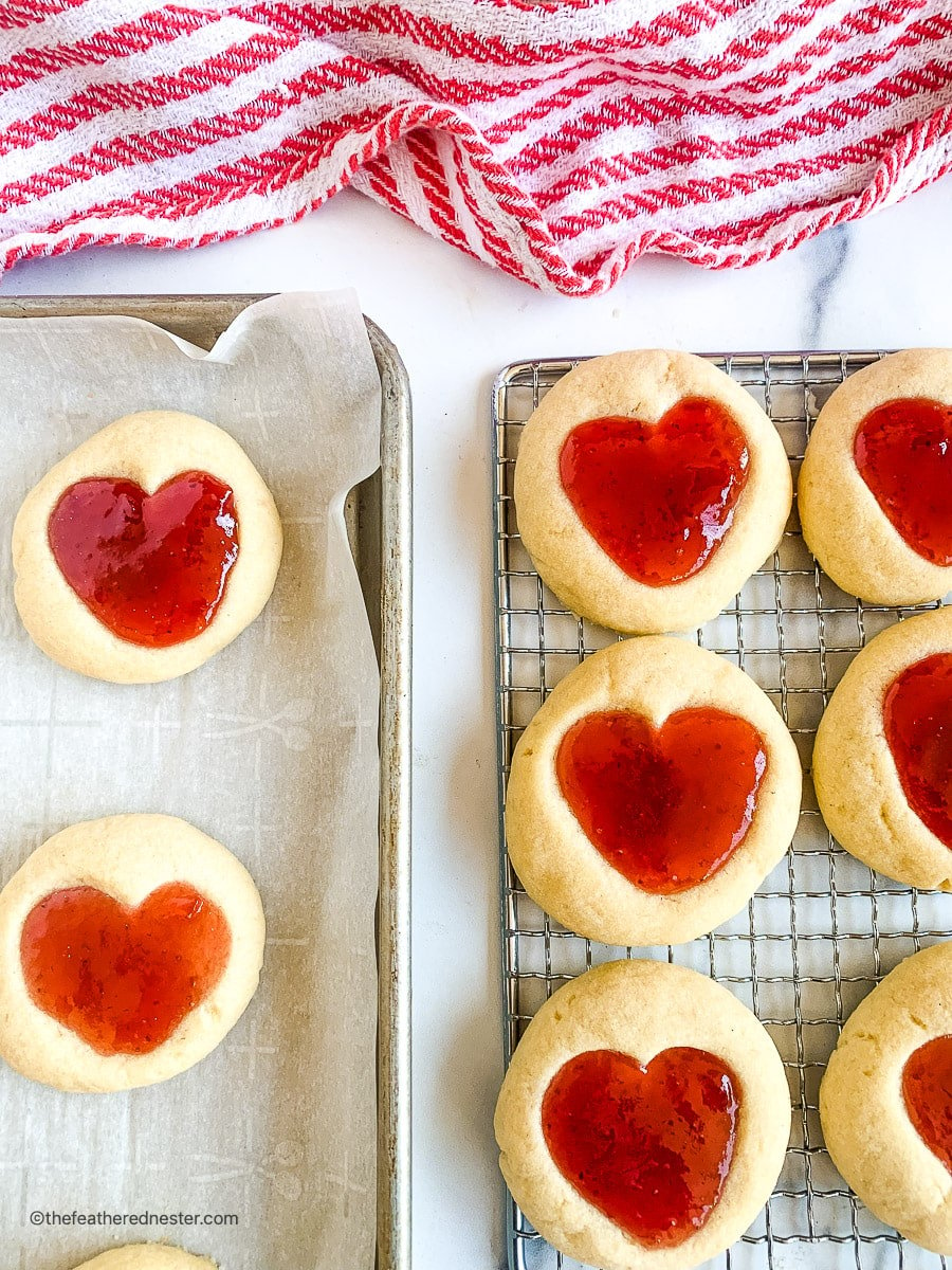 two baking sheets with Valentine cookies, with some on a cooling rack.