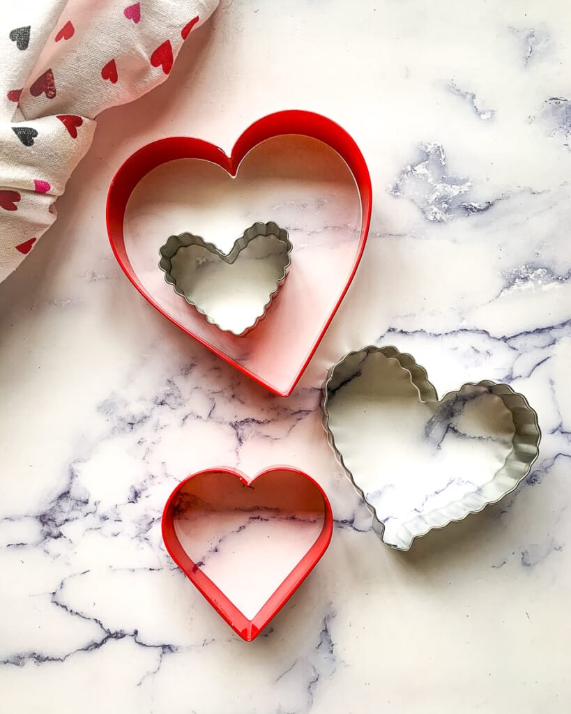 Heart shaped cookie cutters of various sizes on a marble countertop.
