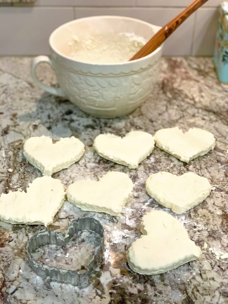 Unbaked heart shaped biscuits on a lightly floured countertop.