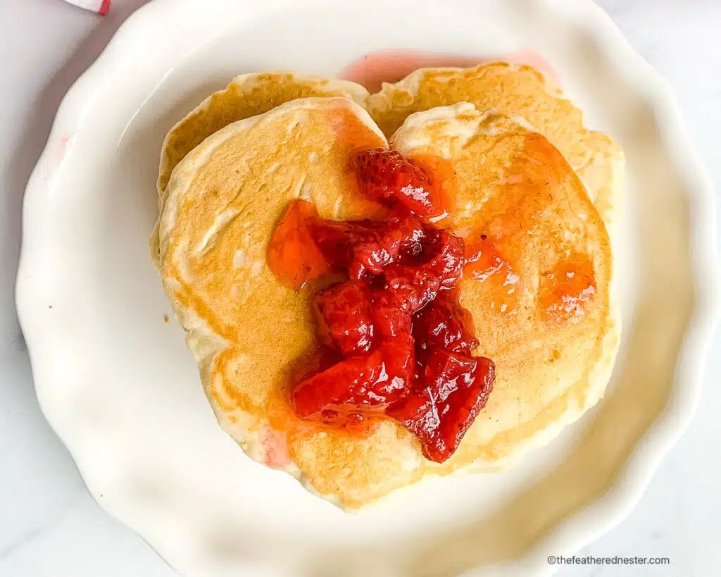 Plated serving of heart shaped pancakes with homemade strawberry syrup.