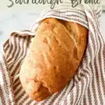 A bread wrapped with dish towel with writings on top that says, "How to store sourdough bread" and writings on the bottom part that says, "www.TheFeatheredNester.com"