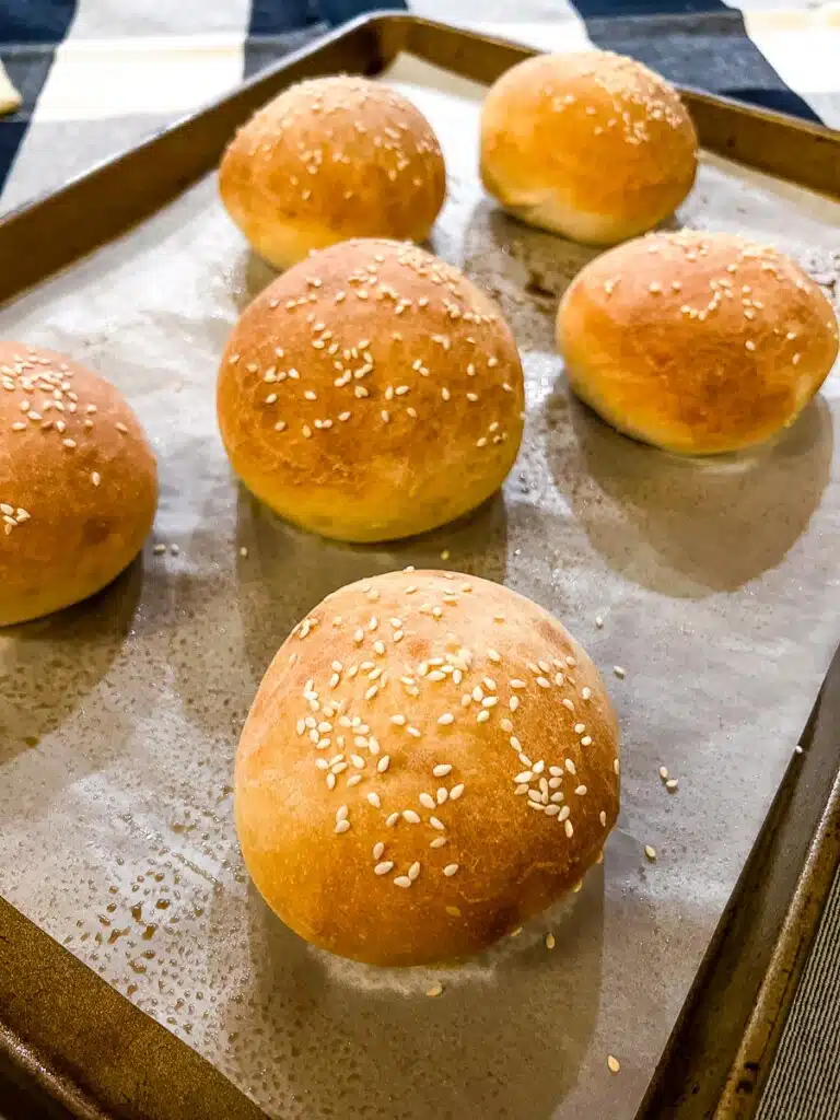 Golden brown sesame seed bun on parchment lined baking sheet.