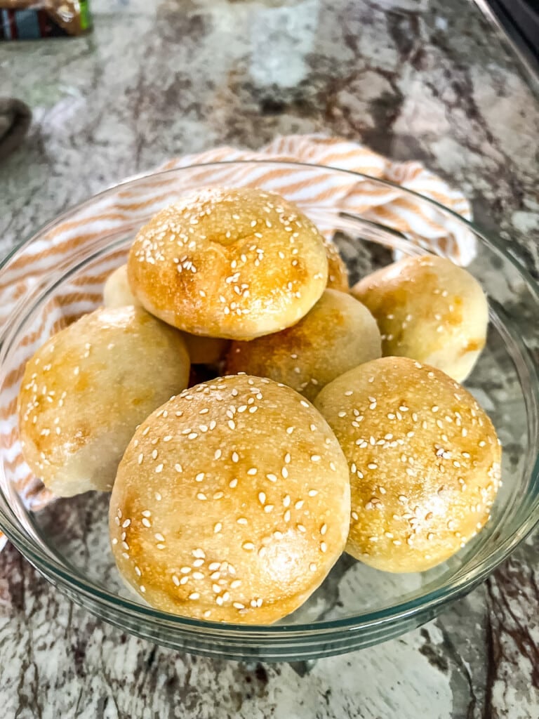 Freshly baked homemade sesame seed buns in a bowl.