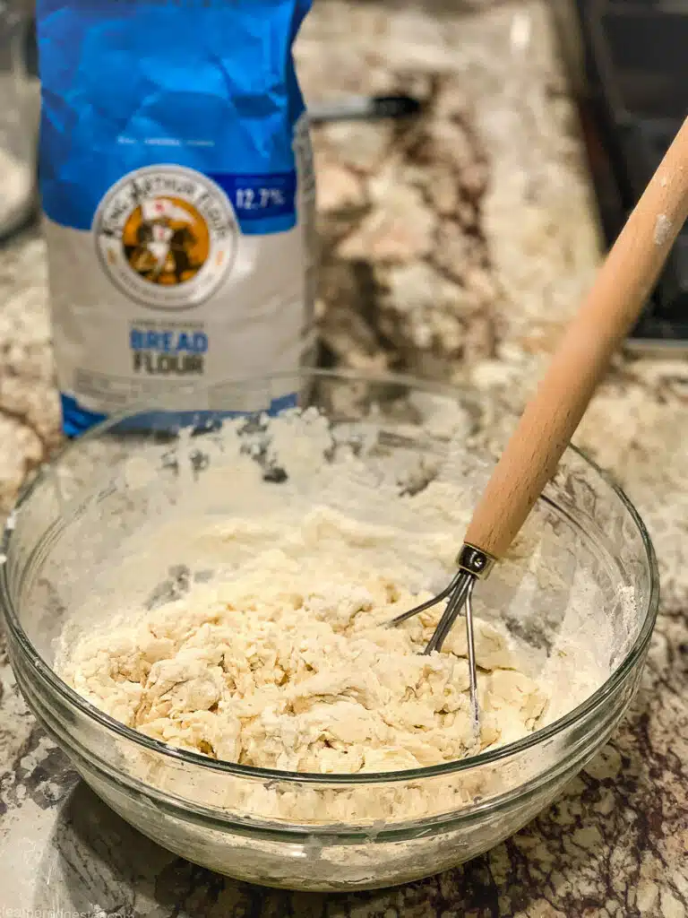 whisking bread flour with warm water and sugar in a mixing bowl.
