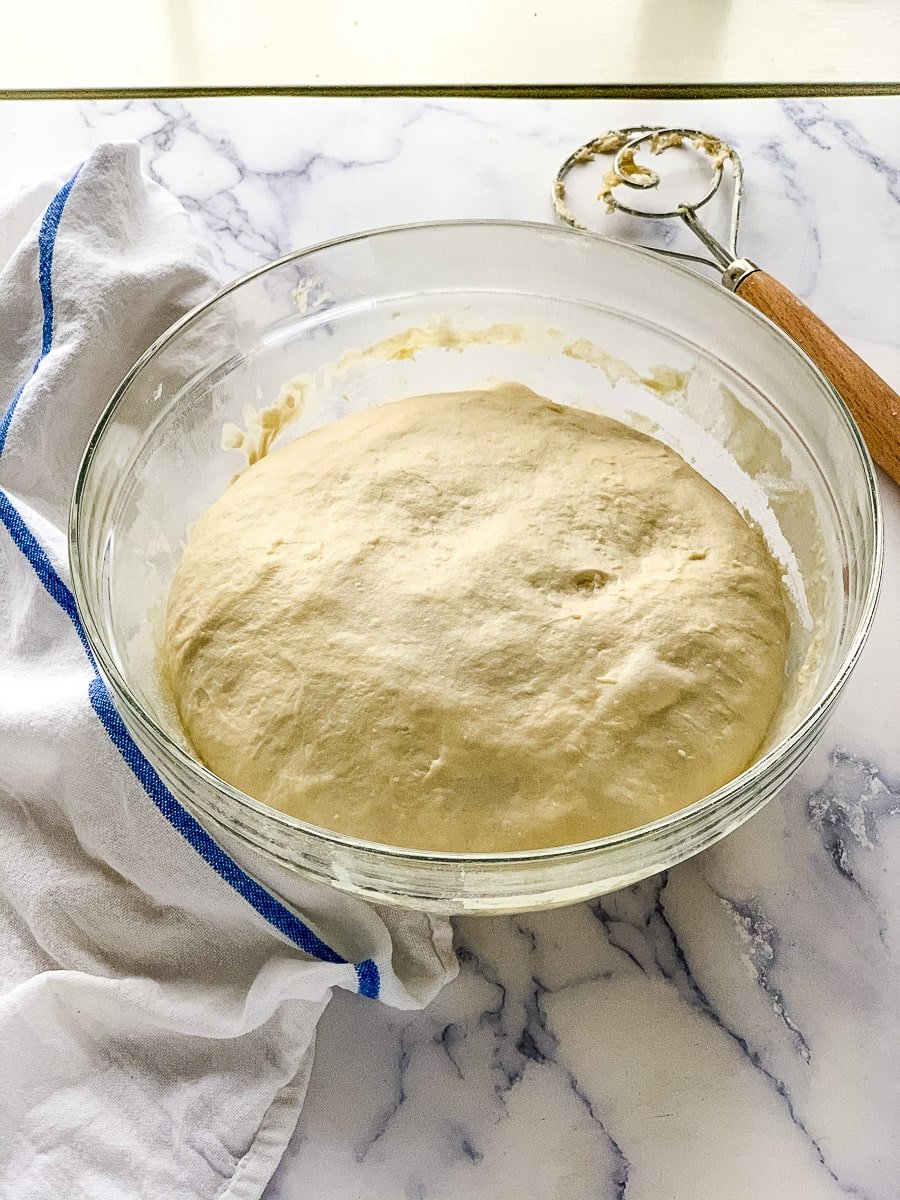 Dough rising in a glass bowl for a sourdough buns recipe.