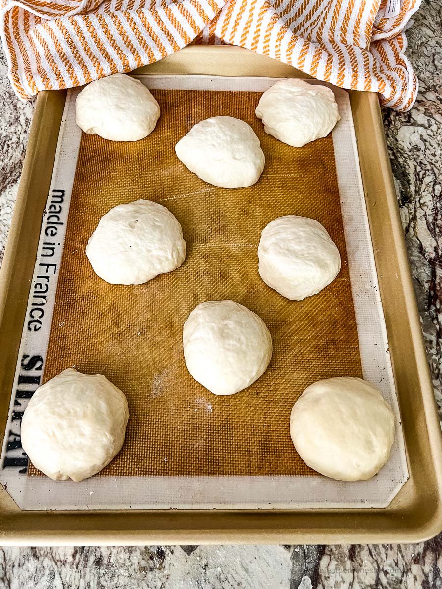 Eight balls of dough on a rimmed sheet pan lined with a silicone baking mat.