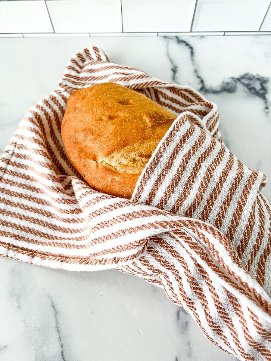 Storing sourdough bread in a brown and white striped kitchen towel.