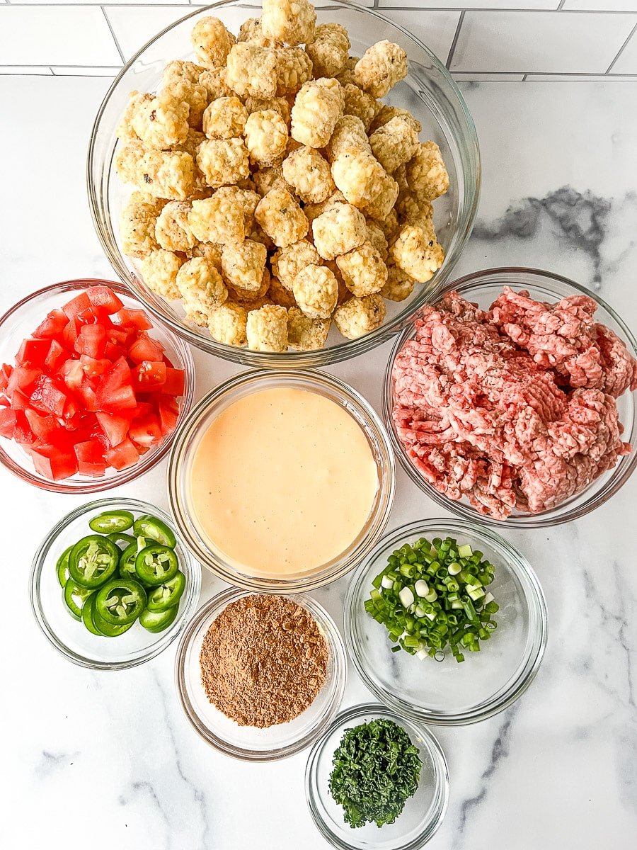 Glass bowls of ground beef, frozen tater tots, cheese sauce and toppings for loaded tater tots.