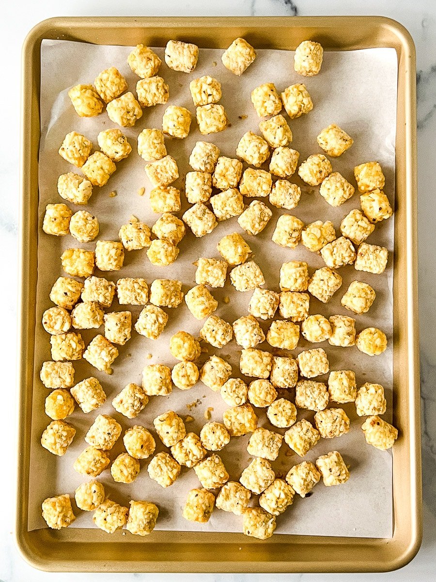 Frozen tater tots on a baking pan lined with parchment paper.