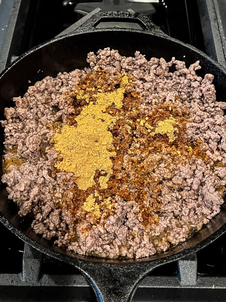 Taco seasoning in a skillet with cooked ground beef for game day snacks.