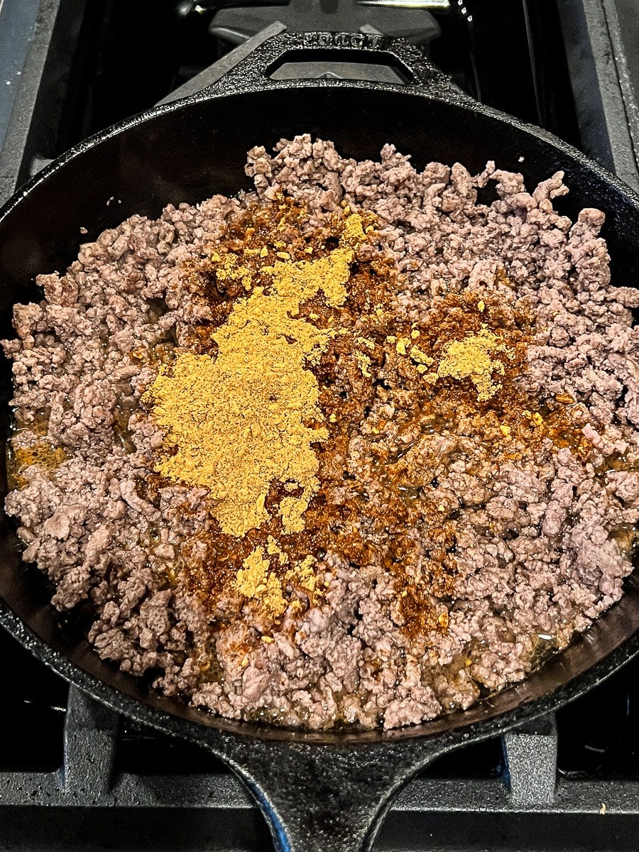 Taco seasoning in a skillet with cooked ground beef for game day snacks.