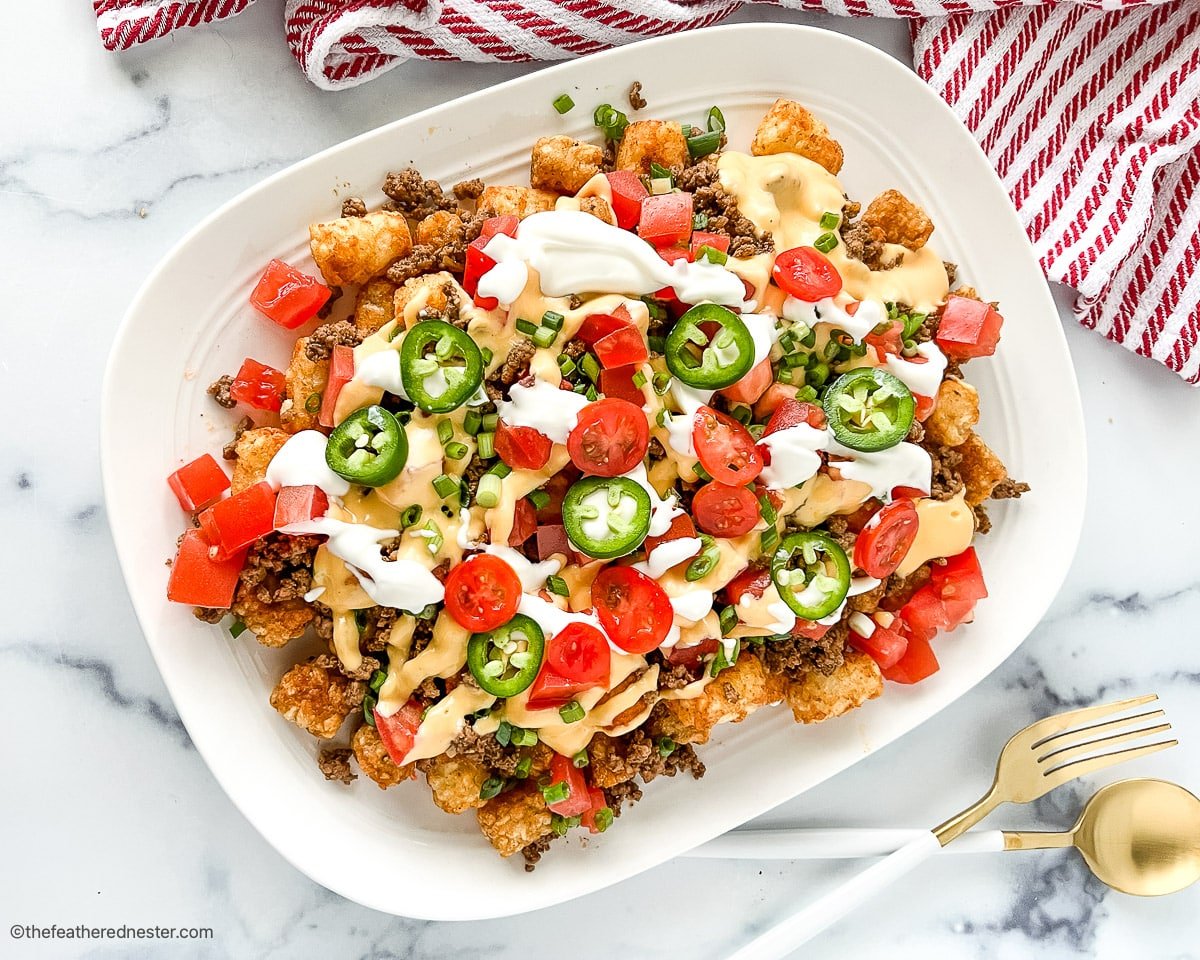 A plate of Tachos, Loaded tater tots topped with jalapeno and sauce