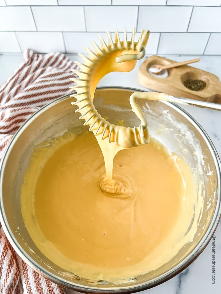 Creamy melted cheddar cheese in a bowl and on a whisk.