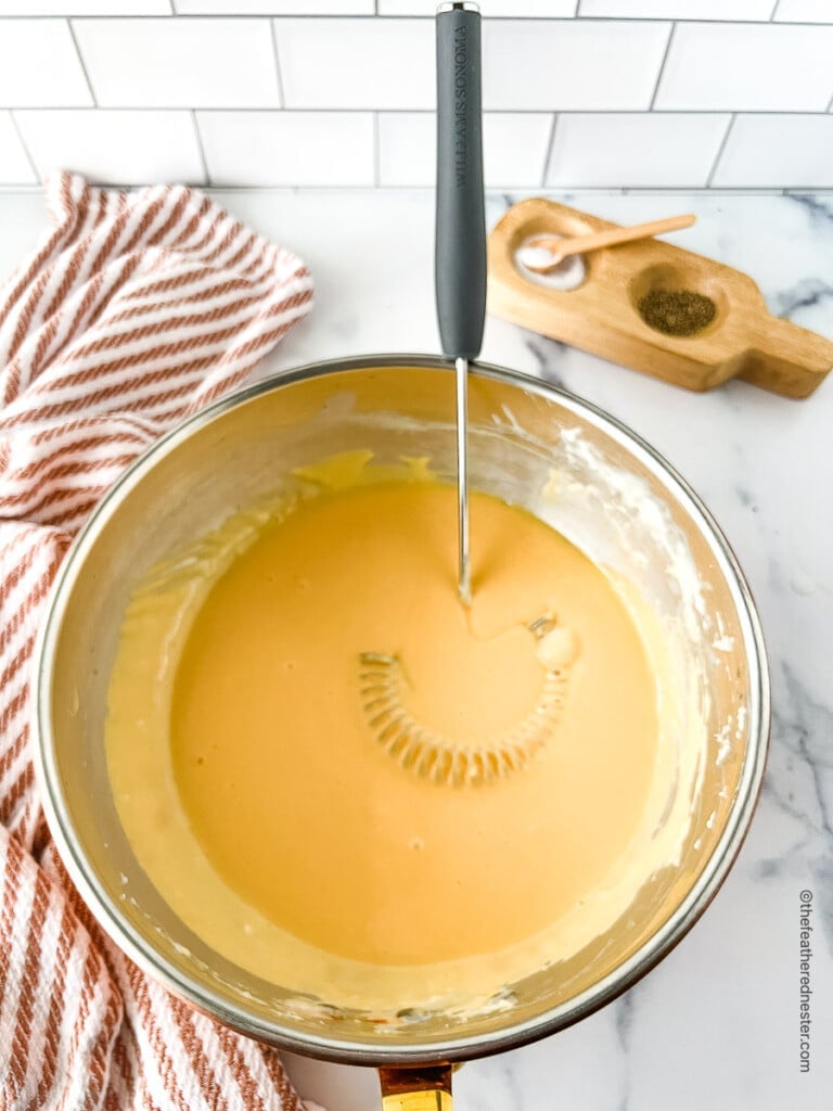 Creamy yellow sauce in a large bowl with a whisk.