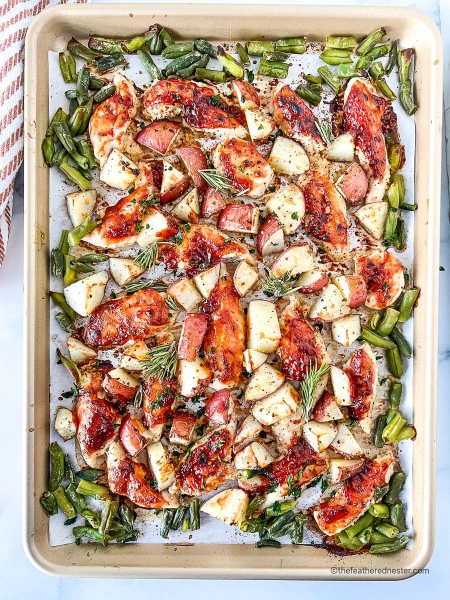 Oven baked BBQ chicken tenders on a baking sheet with roasted vegetables.