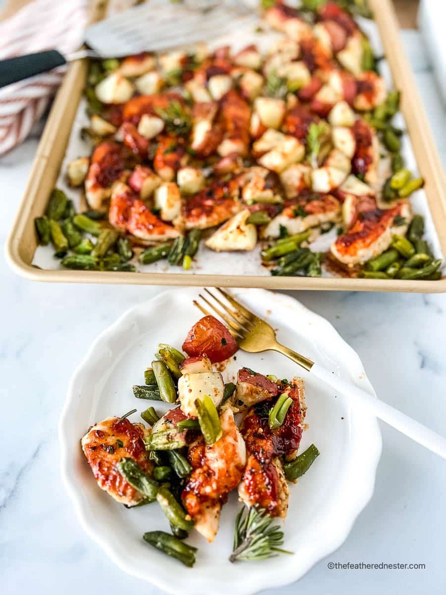 Plate of BBQ chicken tenders with green beans and potatoes in front of a sheet pan dinner.