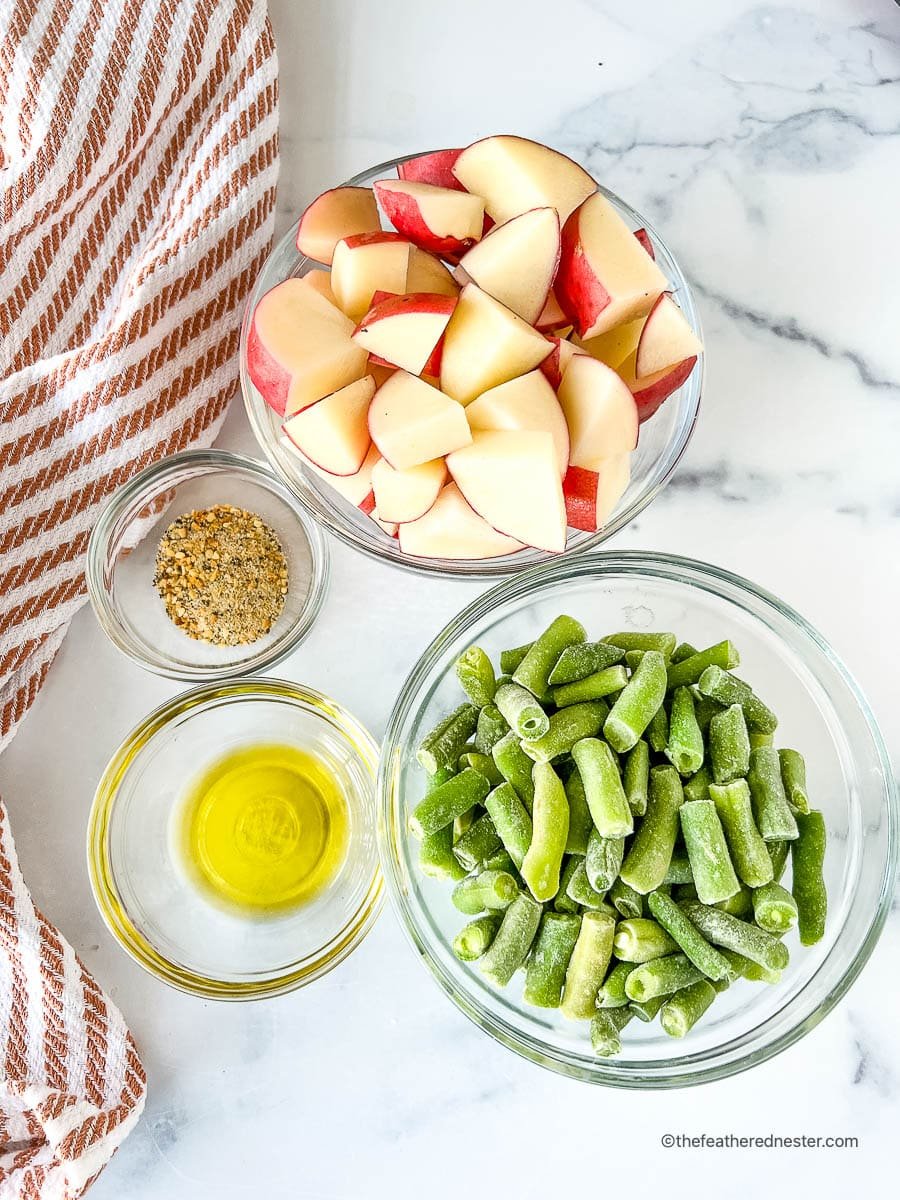 Bowls of seasoning, olive oil, diced potatoes and green beans on a countertop.