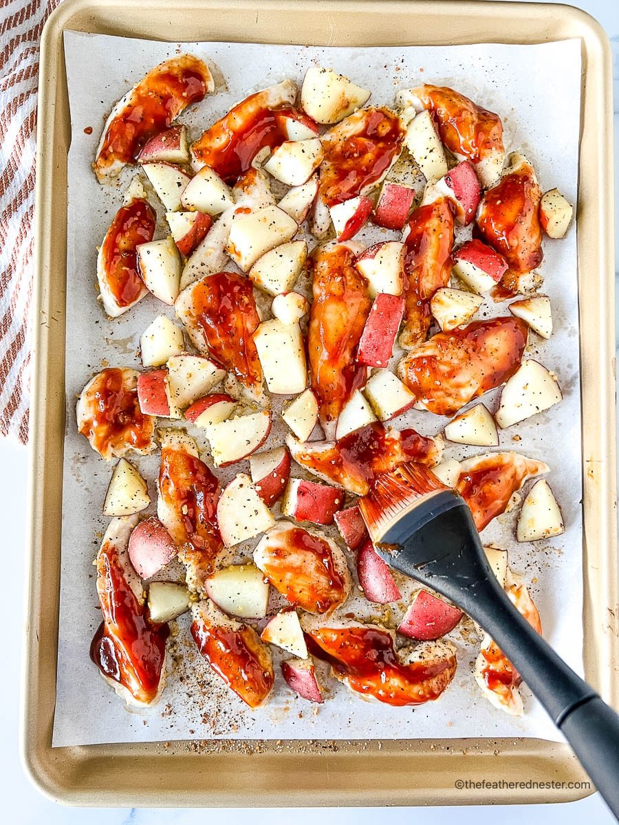 Preparing a chicken sheet pan recipe by basting the chicken strips with BBQ sauce.