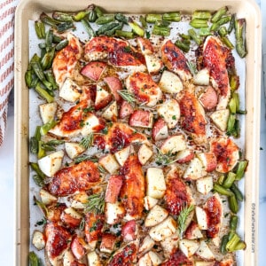 Baked chicken tenderloins coated in barbecue sauce on a baking sheet with roasted green beans and potatoes