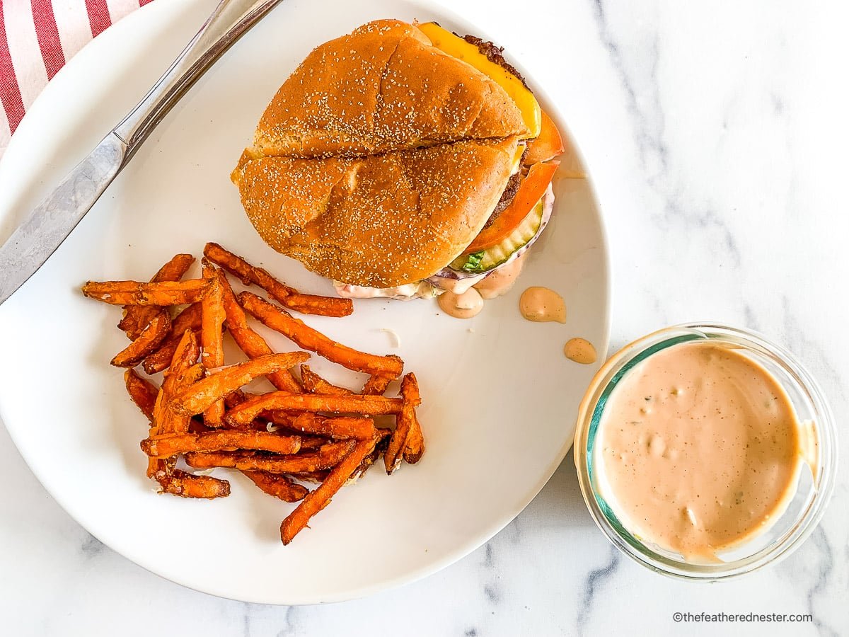 Plated burger and fries next to a small bowl of In n Out sauce.