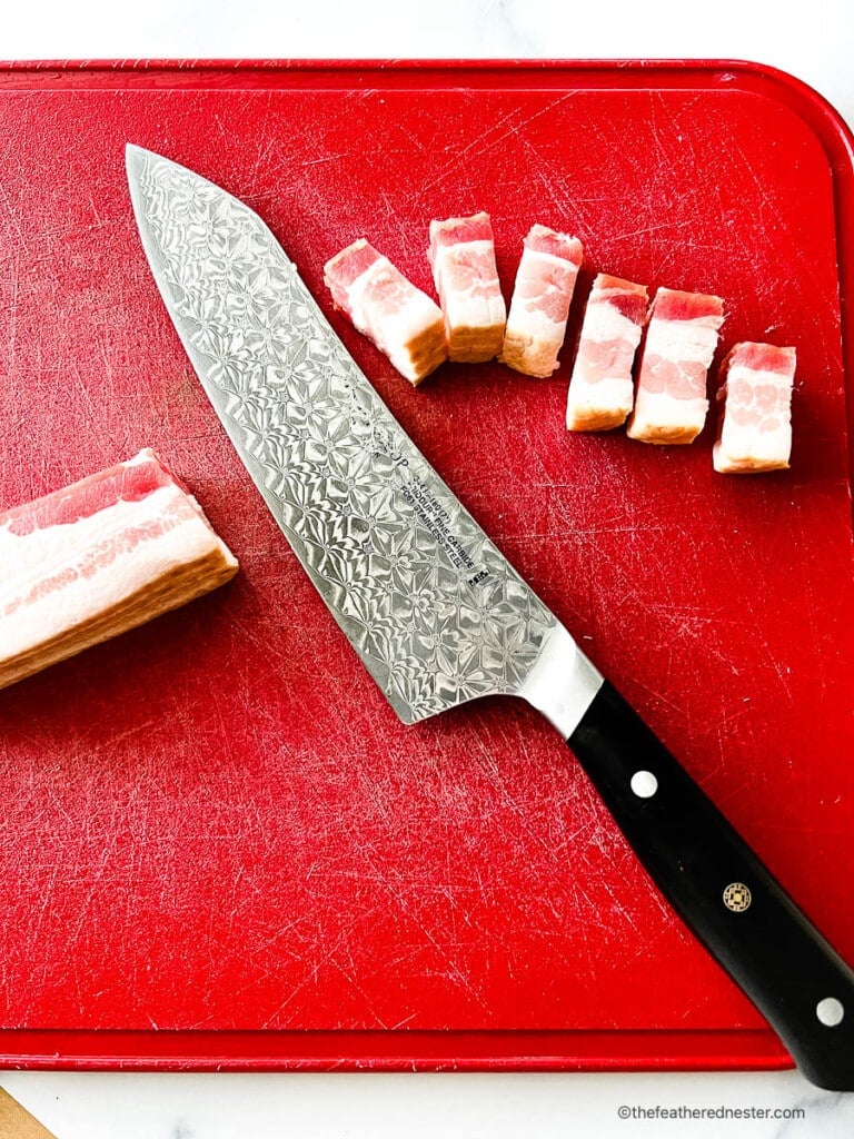 Thick cut bacon and a Chef's knife on a red cutting board