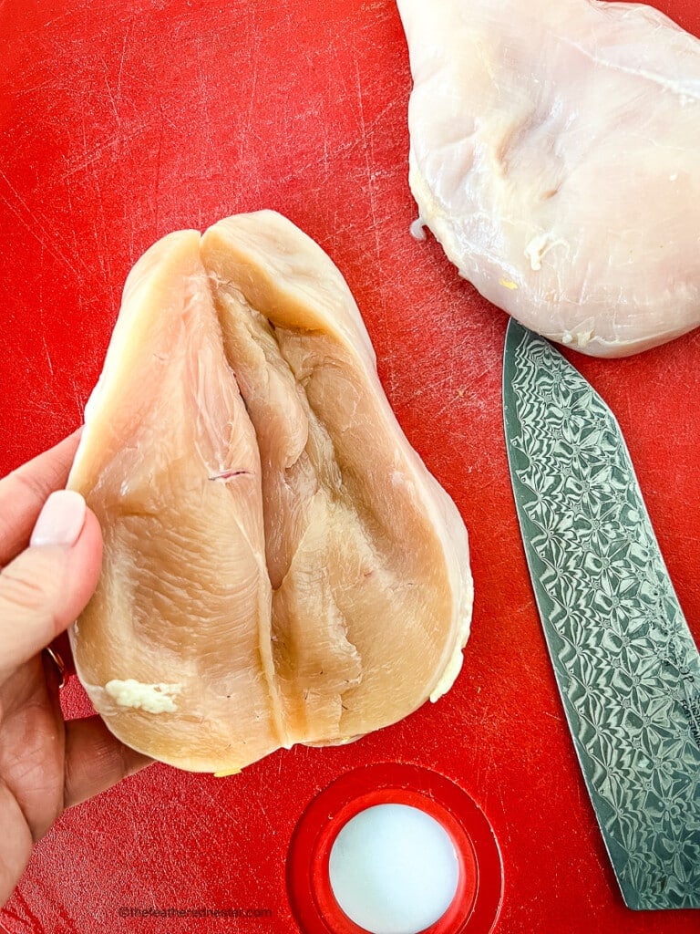 Chef's knife and two pieces of raw poultry on a cutting board