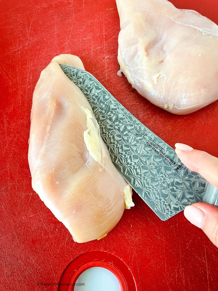 Butterflying chicken breast on a red cutting board.