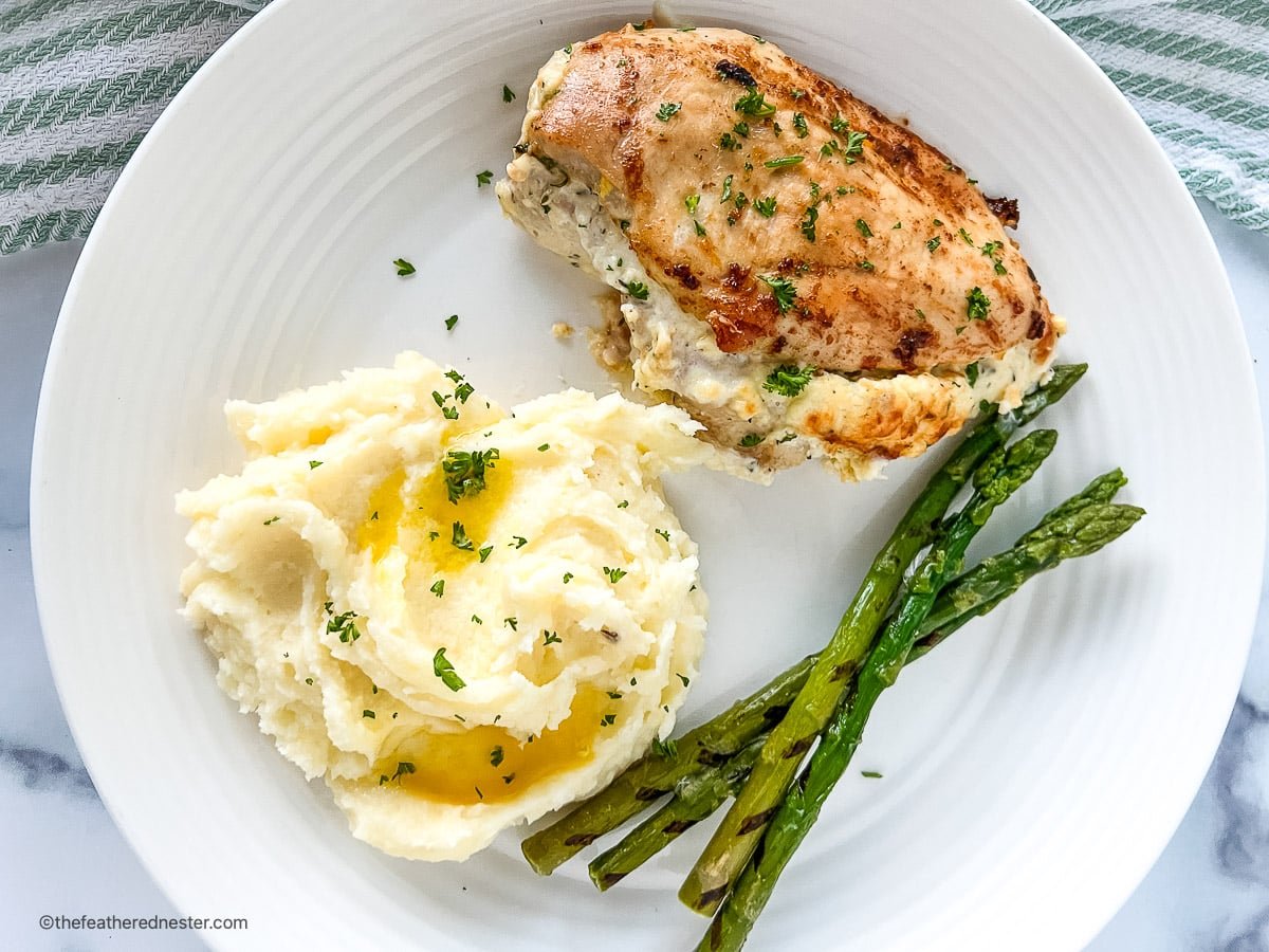 A plate of stuffed chicken with mashed potato and asparagus