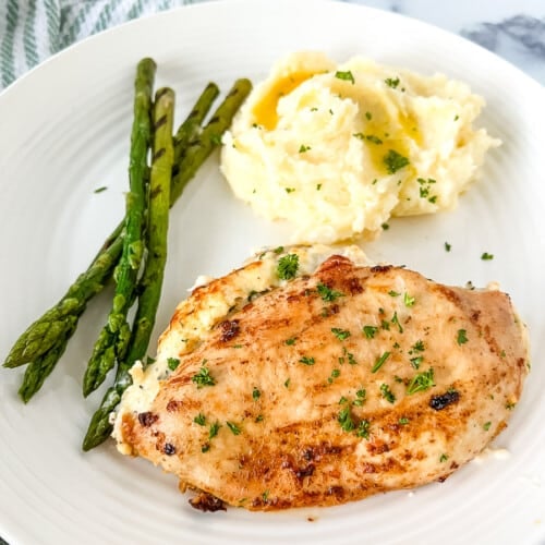 Ruth Chris stuffed chicken on a white dinner plate with mashed potatoes and green vegetables.