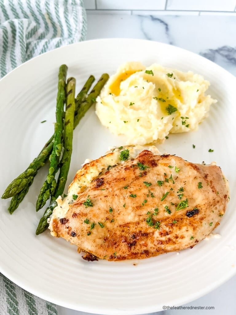 Ruth Chris stuffed chicken on a white dinner plate with mashed potatoes and green vegetables.