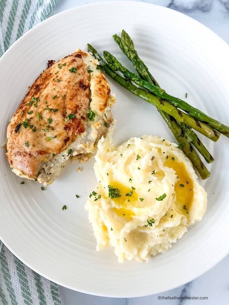 Cheese stuffed chicken breast on a dinner plate with asparagus and fluffy mashed potatoes with gravy.