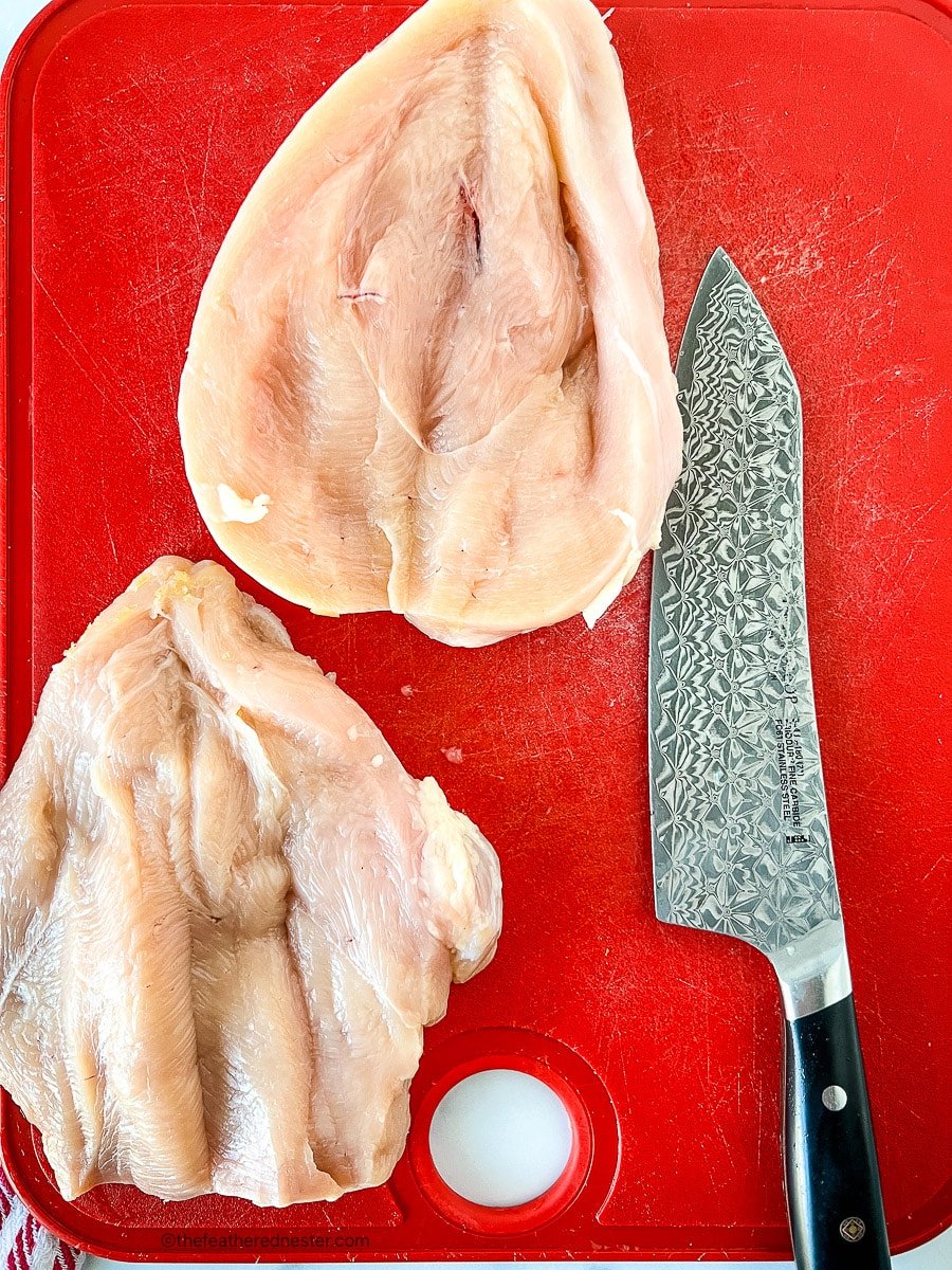 Sharp knife on a red cutting board with raw poultry.